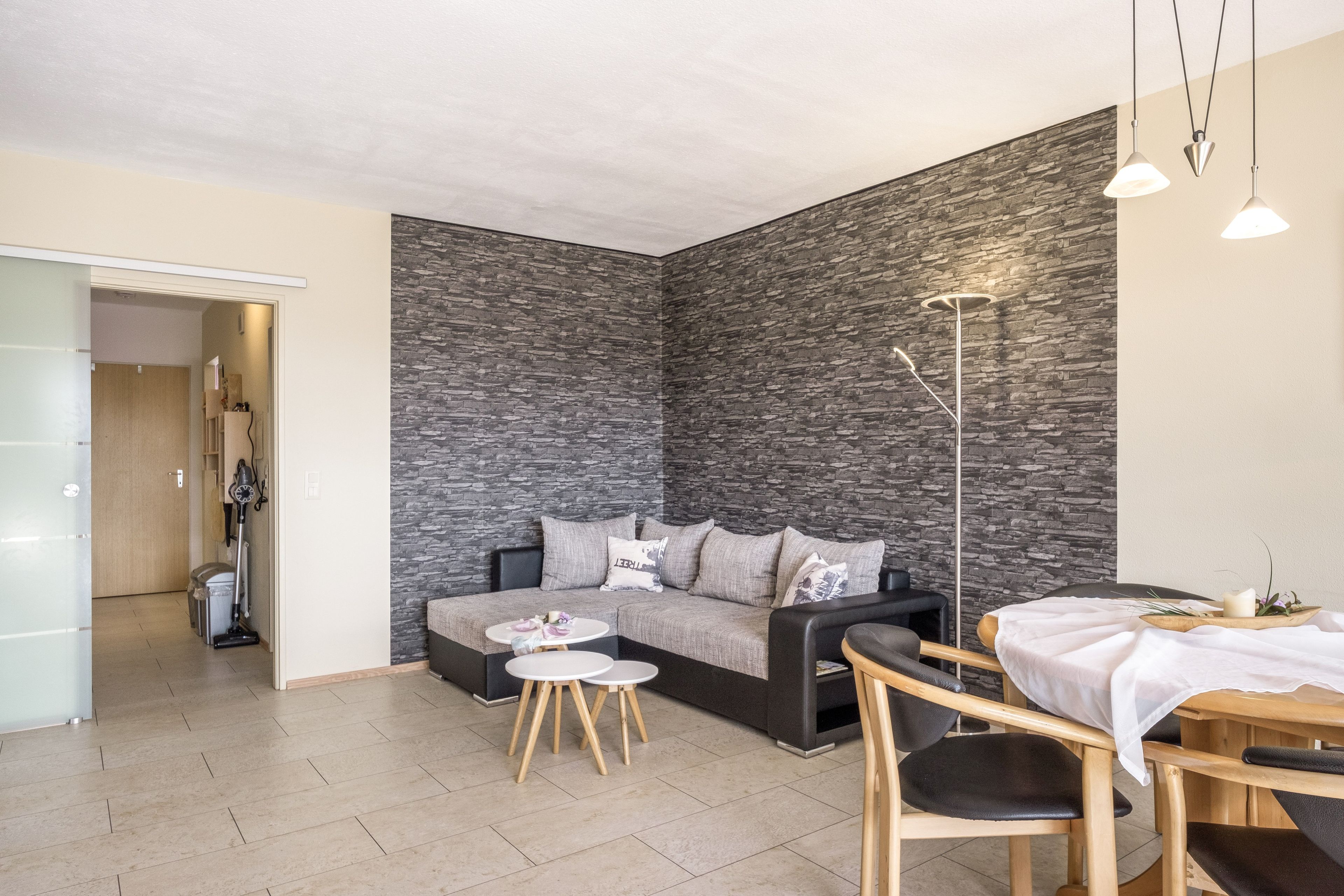 Een moderne woonkamer met een stenen muur, een bank, een salontafel en een eethoek met een tafel en stoelen.