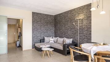 Een moderne woonkamer met een stenen muur, een bank, een salontafel en een eethoek met een tafel en stoelen.