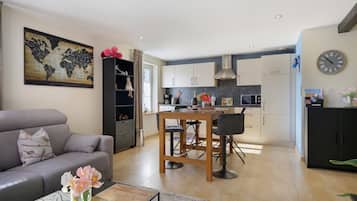 Un salon moderne avec un canapé gris, une table basse ornée d’un vase de fleurs et un coin repas comprenant une table et des chaises en bois.