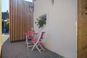 A small outdoor seating area with a table and chairs, a potted plant, and a wooden fence.