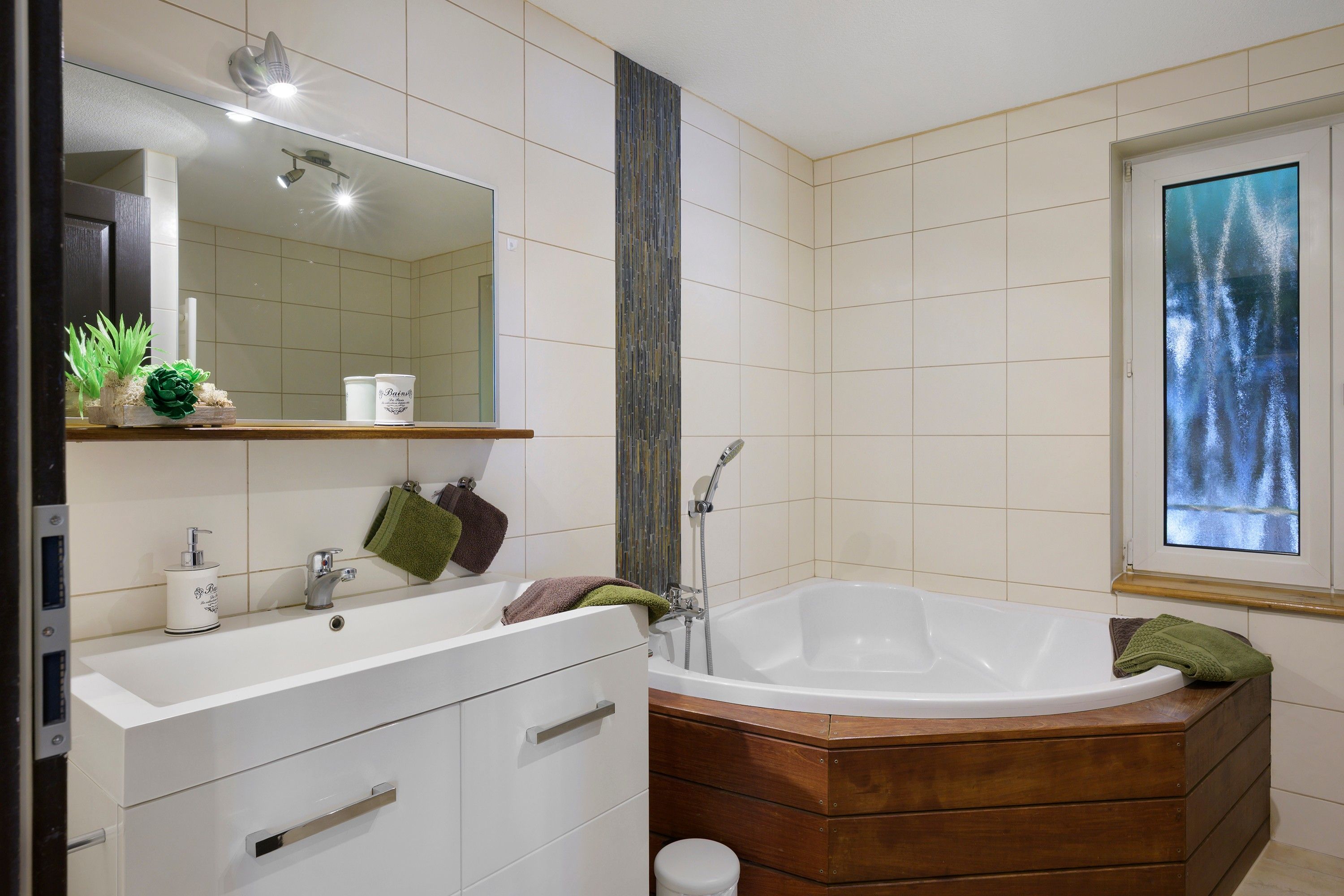 Ein modernes Badezimmer mit einer freistehenden Badewanne, einem Waschtisch mit Spiegel und einem Fenster mit Blick auf Bäume.