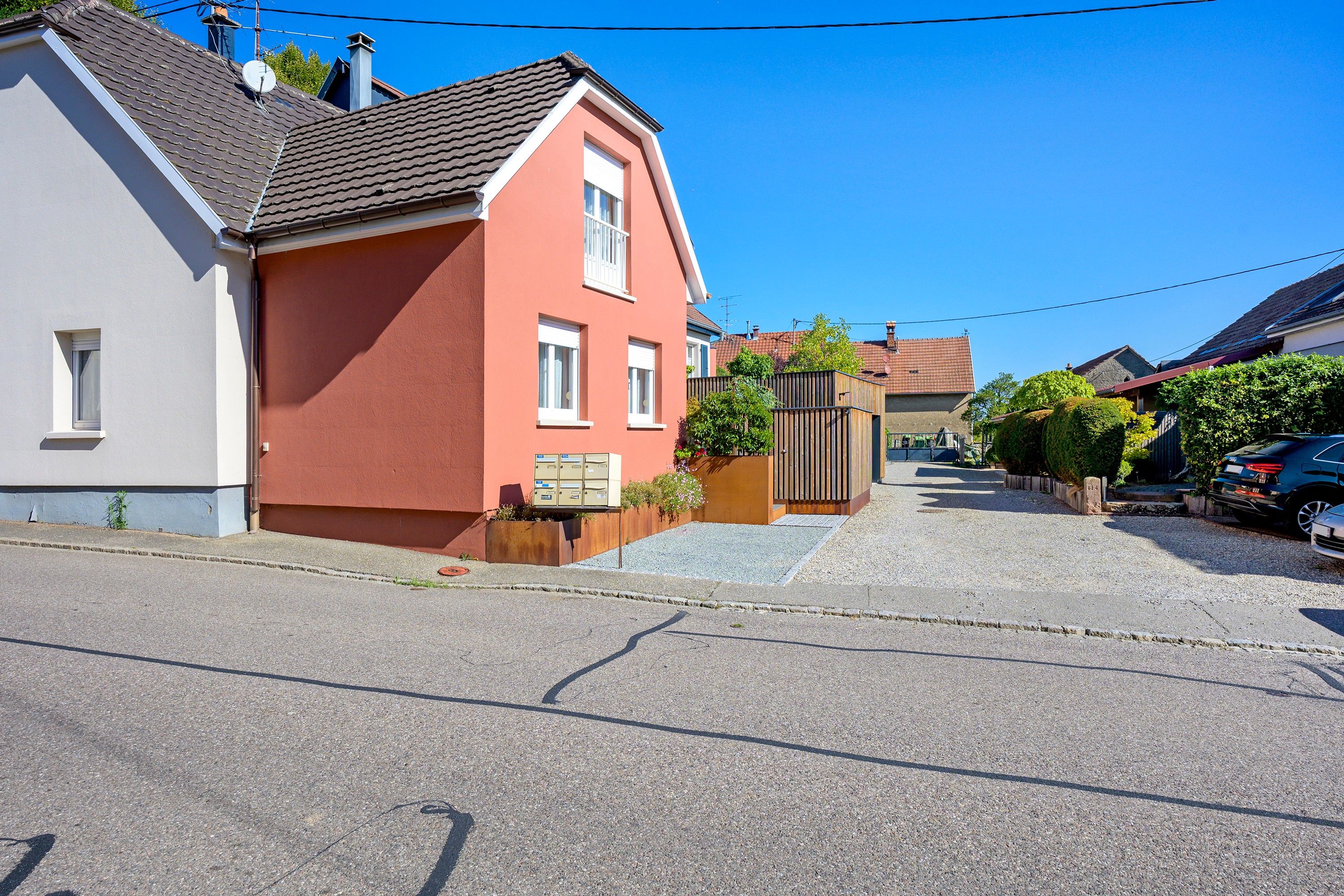 Una calle residencial con casas, un acceso con portón y coches estacionados.