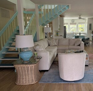 A living room with a sofa, a round ottoman, a glass coffee table, and a wicker side table. - Sanibel coastal charm, pool, across street from beach and Sundial-new on market (Sanibel)
