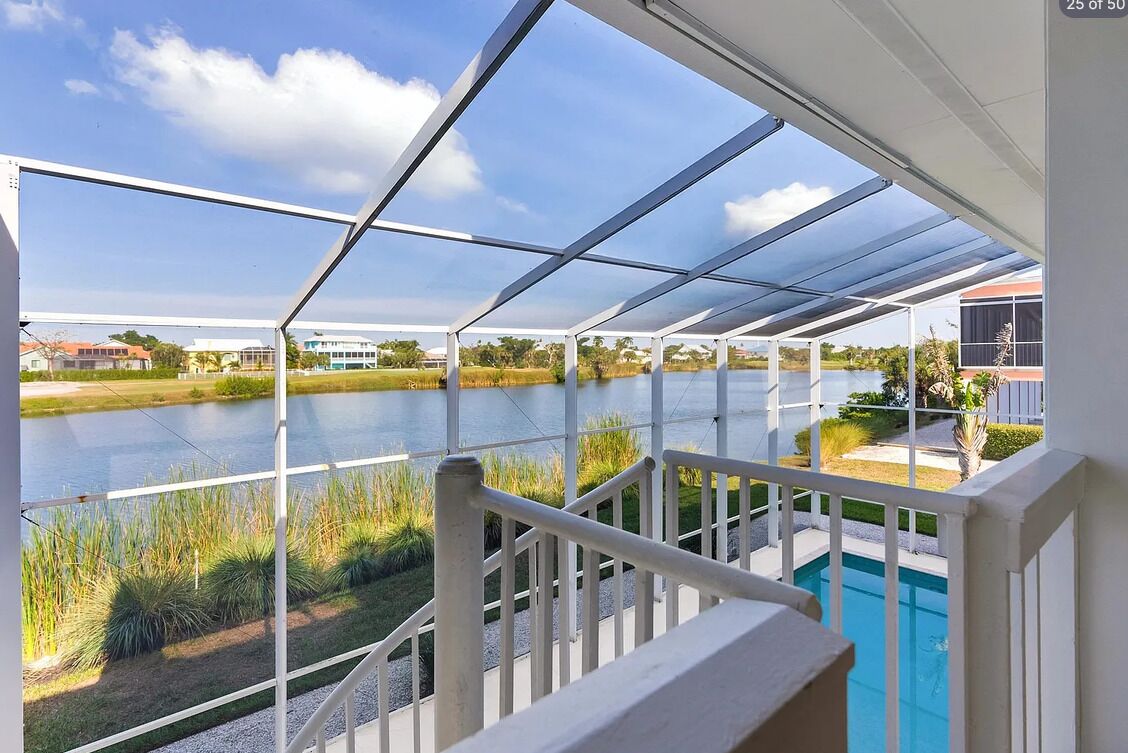 A covered outdoor area with a view of a lake, a pool, and surrounding greenery.