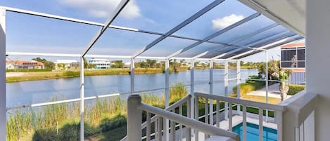 A covered outdoor area with a view of a lake, a pool, and surrounding greenery.