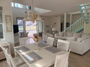 A spacious living area with a white dining table, chairs, and a sofa. A ceiling fan and a staircase are visible in the background. - Sanibel coastal charm, pool, across street from beach and Sundial-new on market (Sanibel)