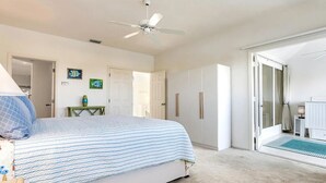 Una camera da letto con un letto, una ventola a soffitto, una porta e vista sul bagno.