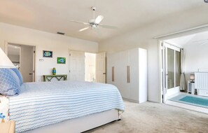 A bedroom with a bed, a ceiling fan, a door, and a view of a bathroom. - Sanibel coastal charm, pool, across street from beach and Sundial-new on market (Sanibel)