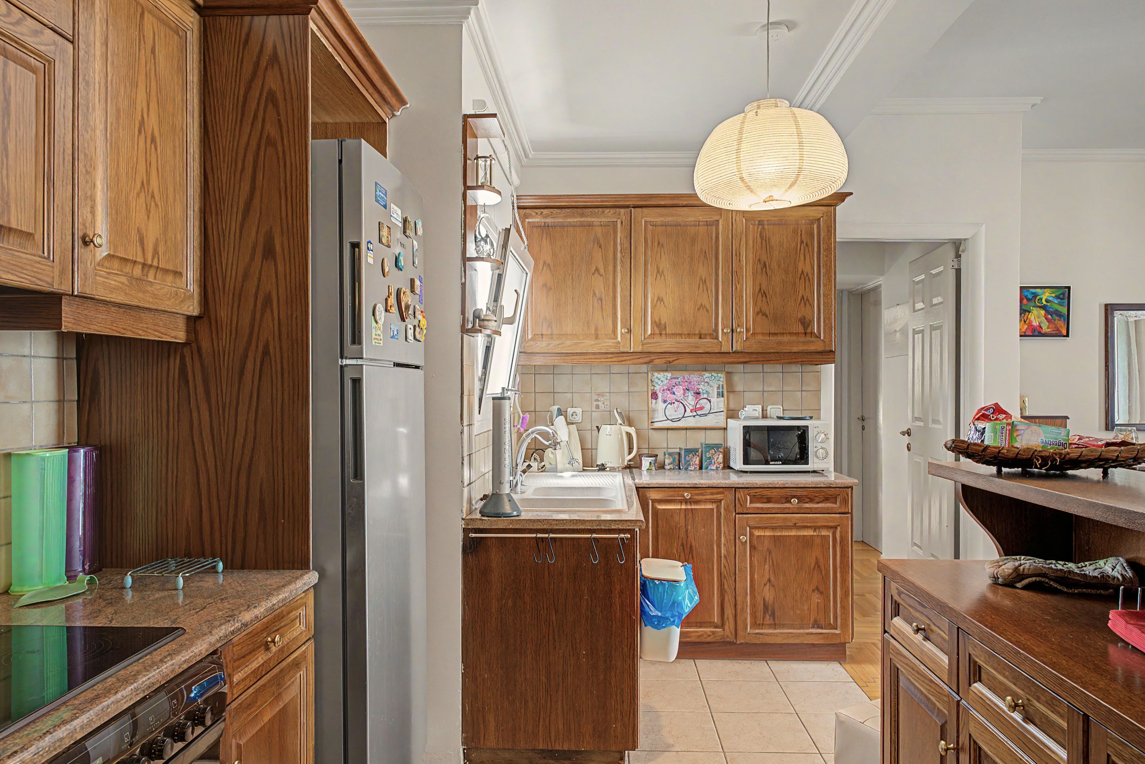A kitchen with wooden cabinets, a stainless steel refrigerator, a microwave, and a hanging light fixture.