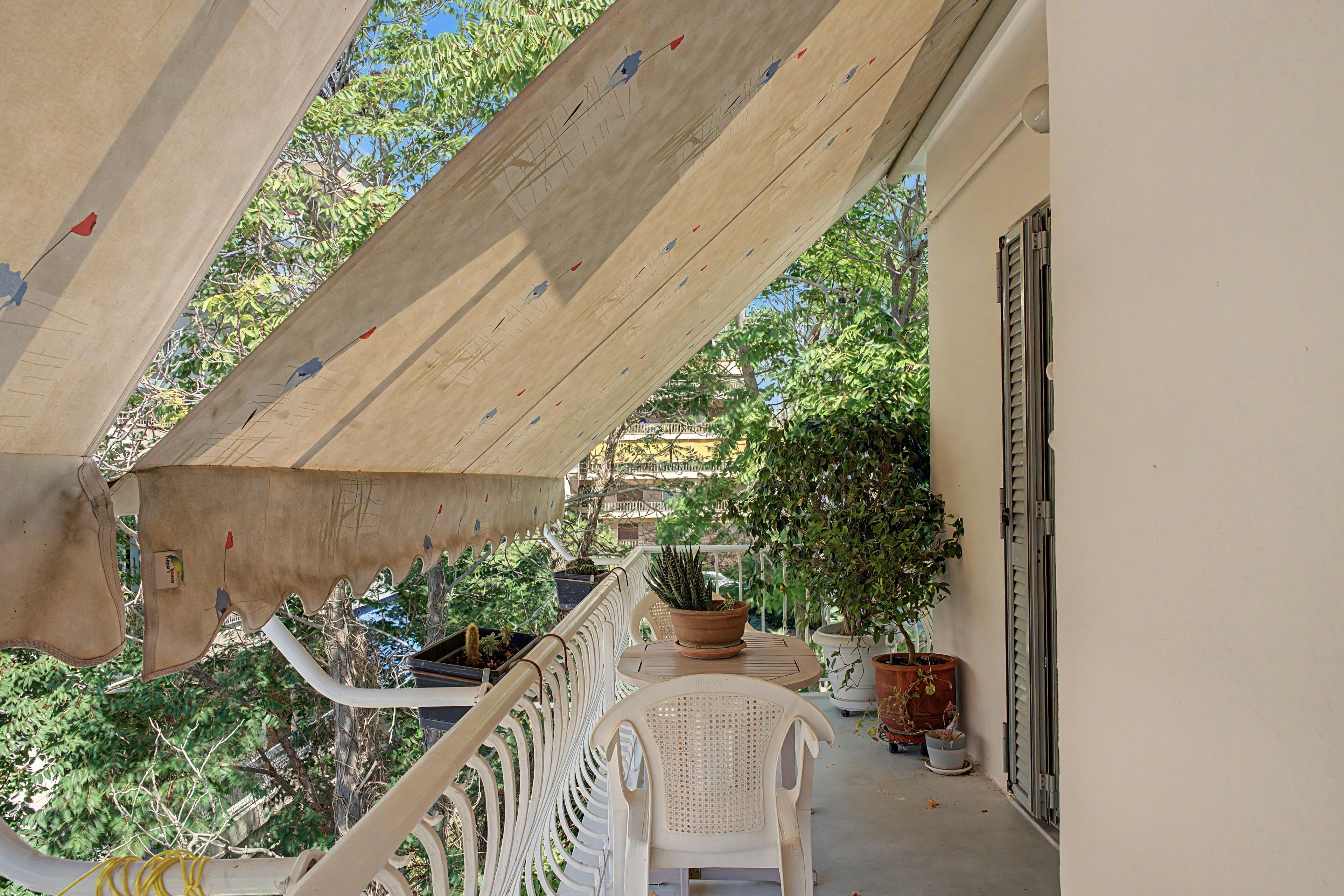 Un balcon doté d’un plafond en bois, de plantes en pot et d’une chaise en plastique blanche.