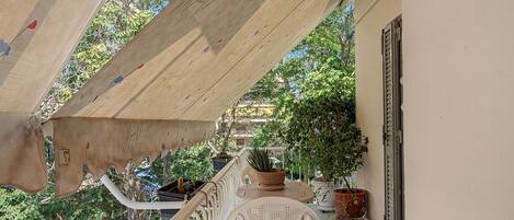 Un balcon doté d’un plafond en bois, de plantes en pot et d’une chaise en plastique blanche.