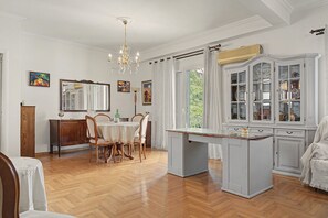 Een eetruimte met een kroonluchter, houten stoelen, een tafel en een kast met glazen deuren.