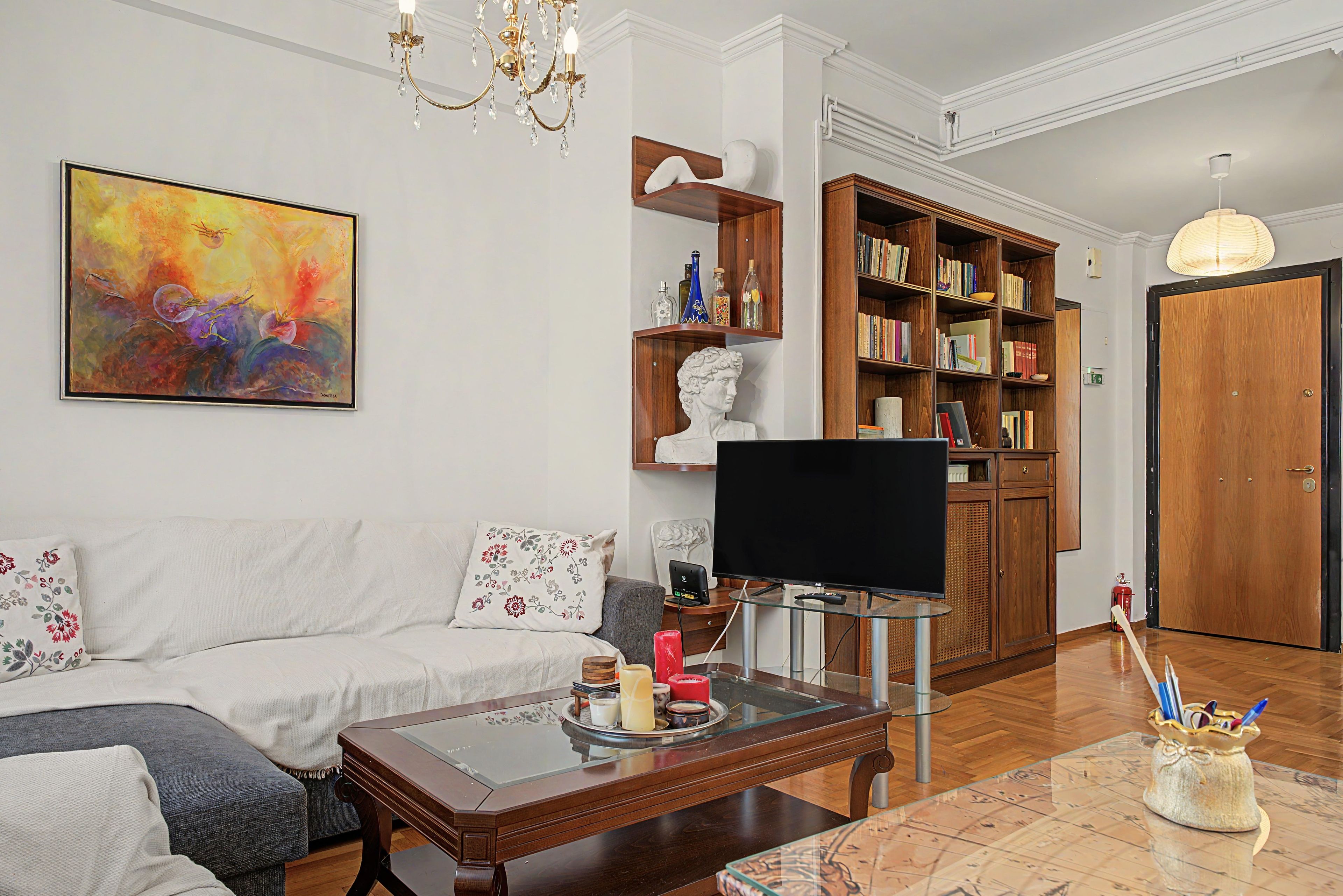A living room with a sofa, coffee table, TV, bookshelf, and a painting on the wall.