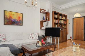 Ein Wohnzimmer mit Sofa, Couchtisch, Fernseher, Bücherregal und einem Bild an der Wand.