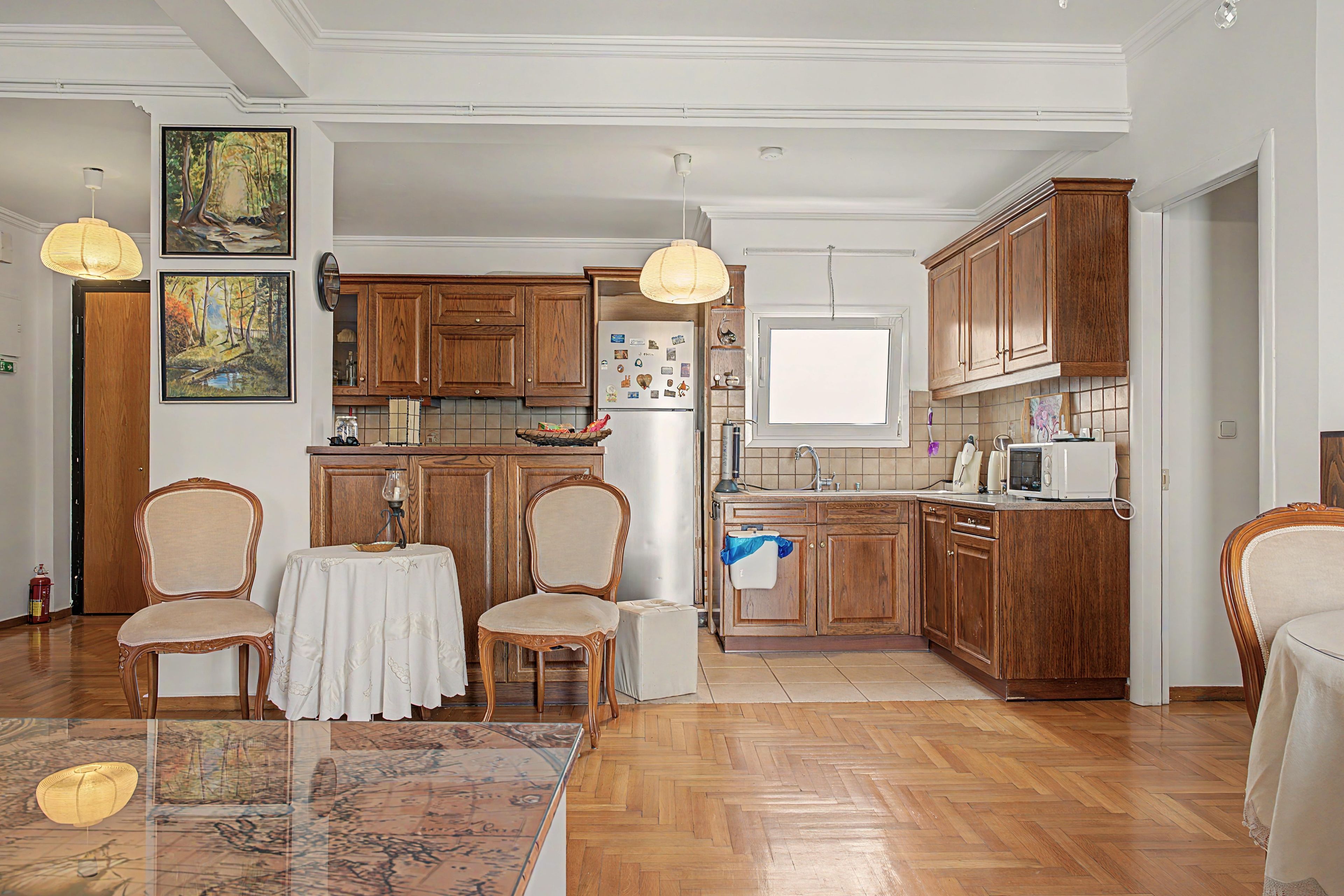 A spacious kitchen with wooden cabinets, a dining area with a table and chairs, and a herringbone-patterned floor.
