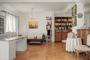 Een ruime woonkamer met een houten vloer, een witte bank, een salontafel en een boekenplank vol boeken.