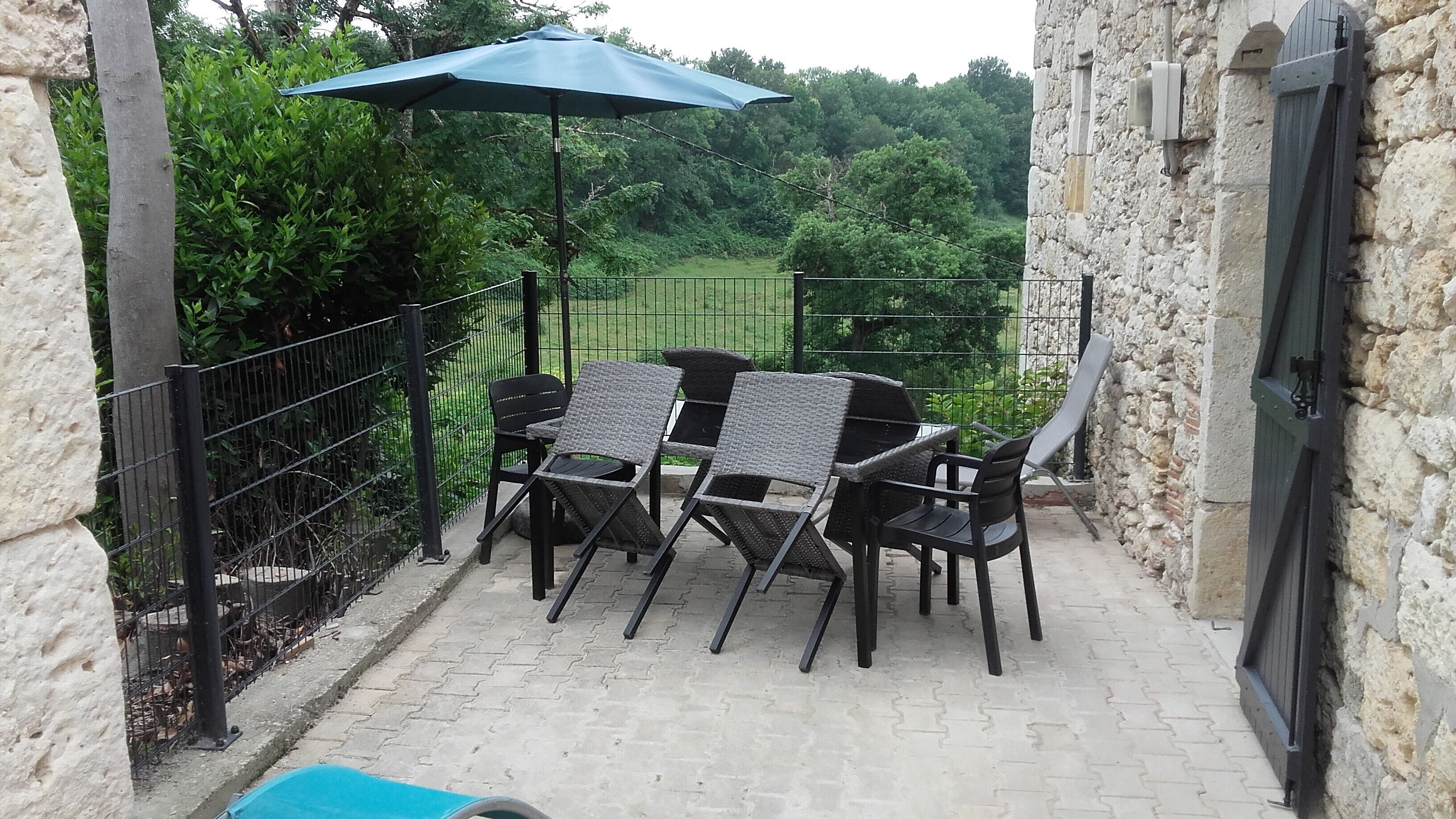 Un patio exterior con una mesa, sillas, una sombrilla azul y un muro de piedra.