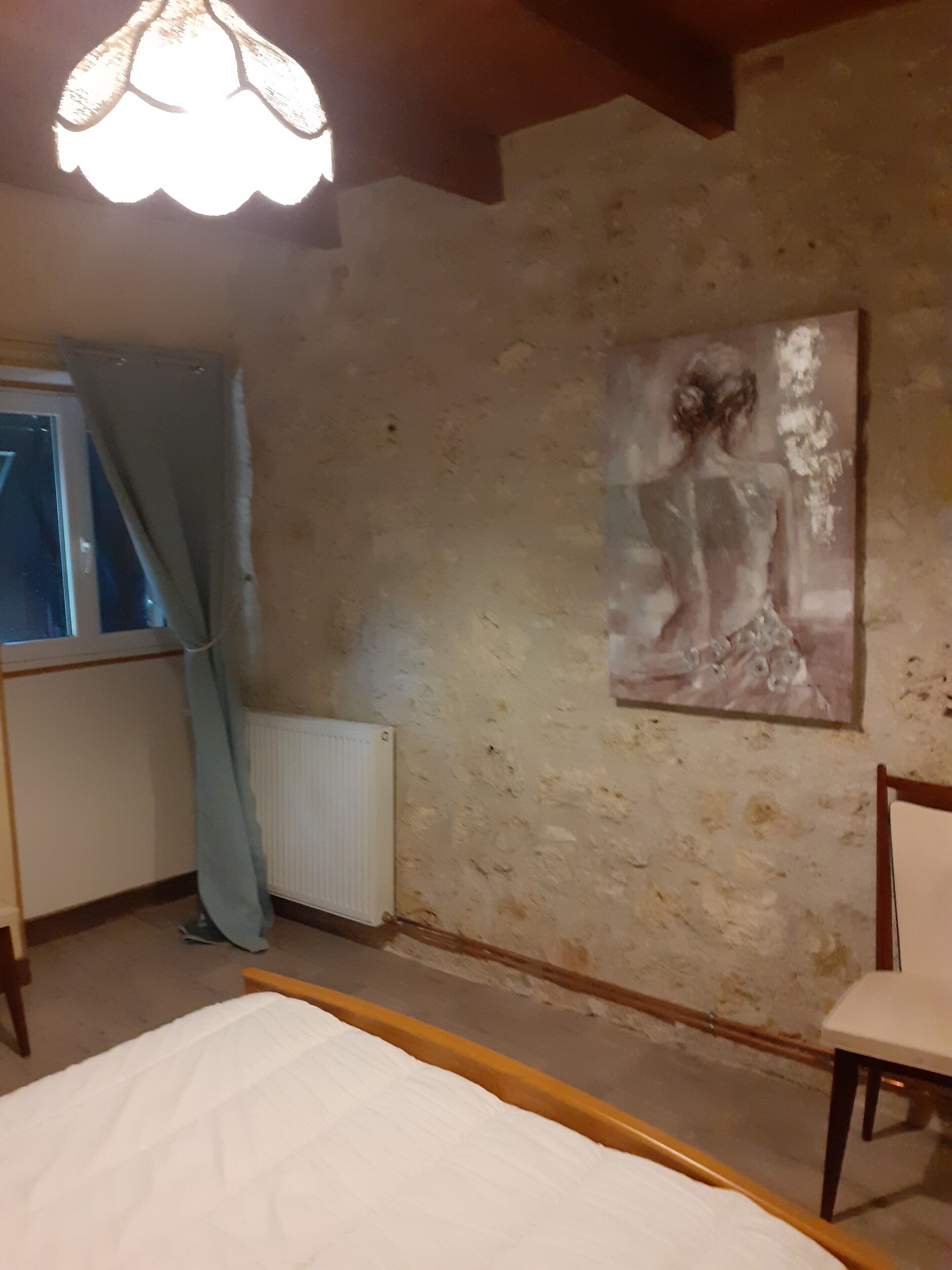 Una habitació amb un llit, una cadira, un radiador i un quadre a la paret.