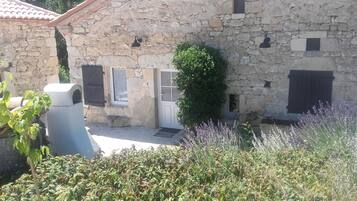 Un edificio de piedra con puerta, ventanas y un pequeño jardín de lavanda.