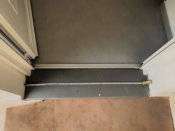 Rincón de una habitación con piso oscuro, marco de puerta blanco y un metro en el suelo.
