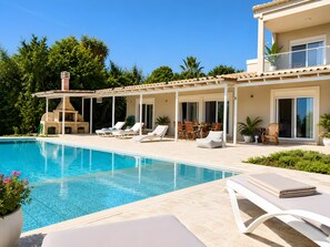 A poolside area with lounge chairs, a barbecue, and a covered patio with a table and chairs.