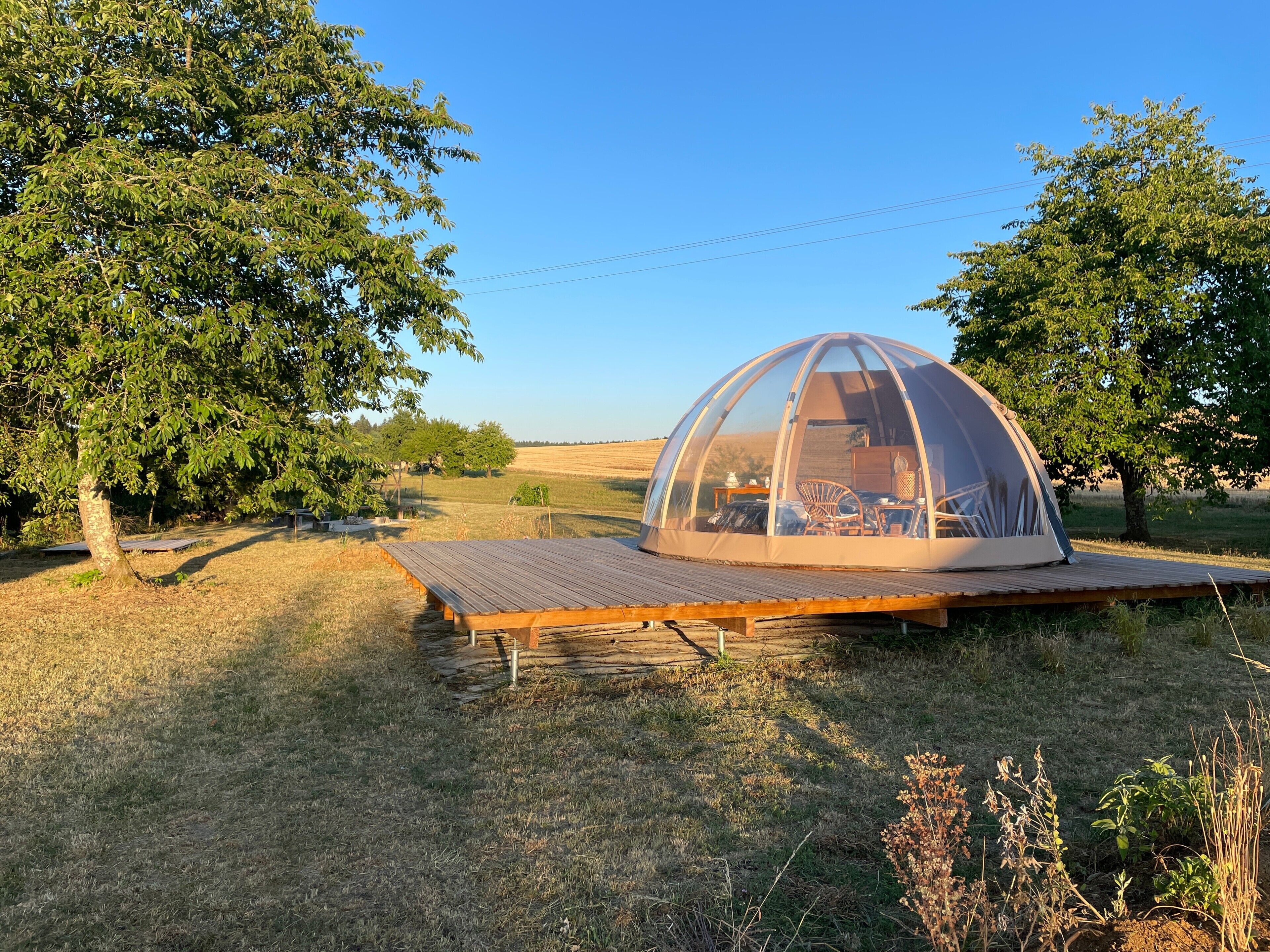 A dome-shaped tent with a wooden deck in a grassy field.