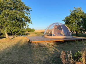 A dome-shaped tent with a wooden deck in a grassy field.
