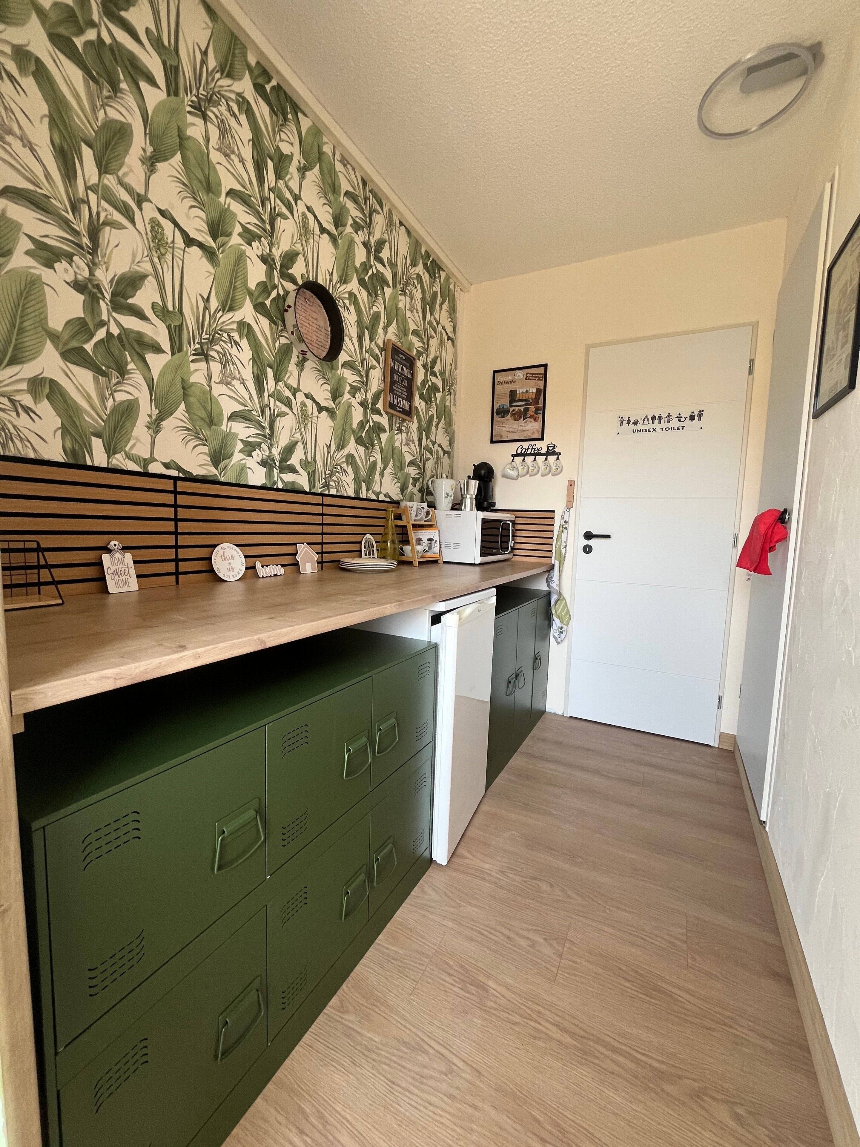 Une cuisine compacte dotée d’un plan de travail en bois, de placards de rangement verts, d’un four à micro-ondes et d’une machine à café.