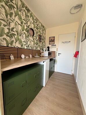 A compact kitchen with a wooden countertop, green storage cabinets, a microwave, and a coffee machine.