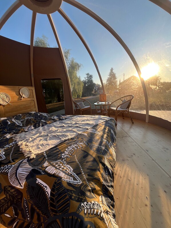 A cozy room with a bed, two chairs, and a table, featuring a patterned bedspread and a view of trees and a building.