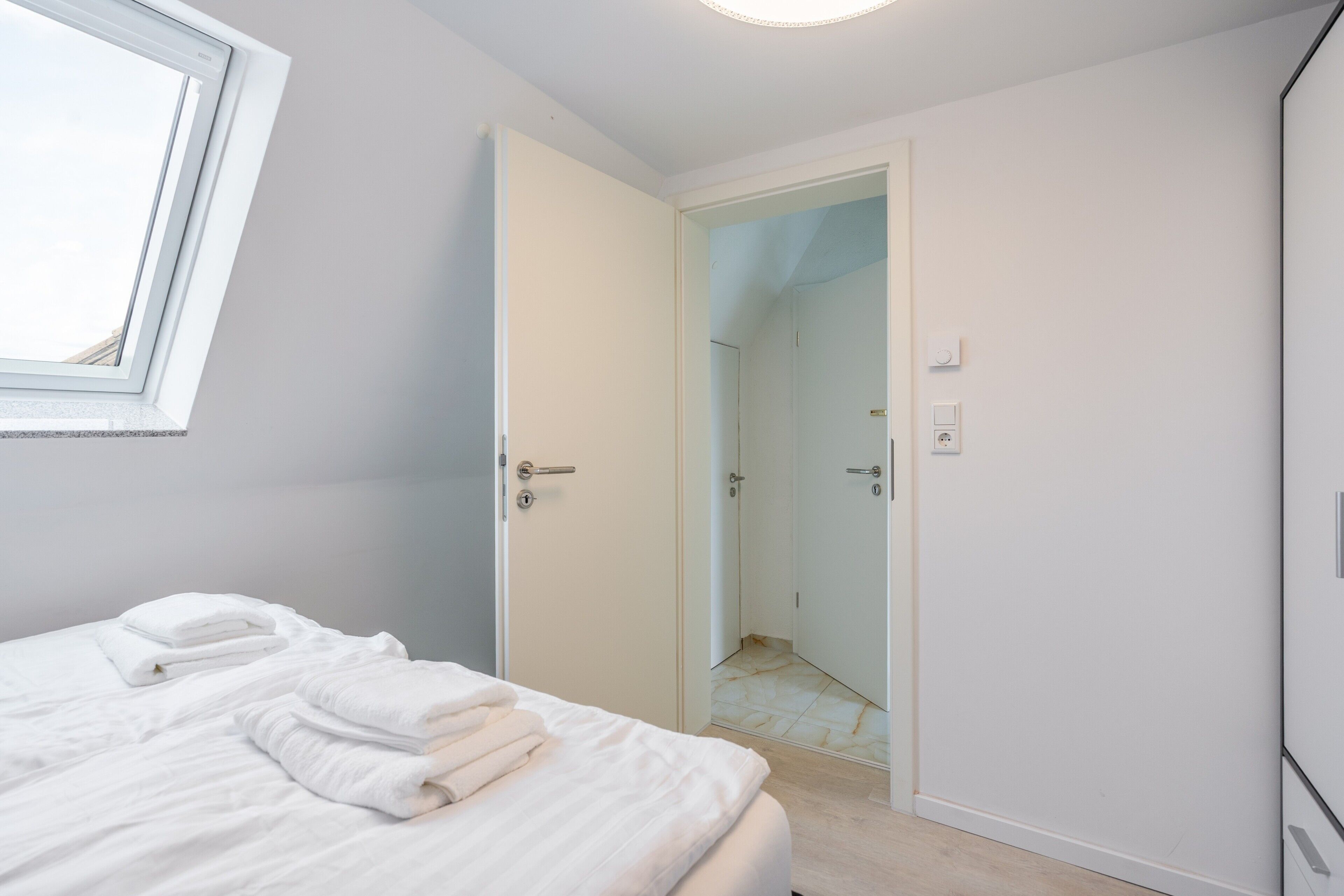 A bedroom with a bed, a window, and an open door leading to a bathroom.