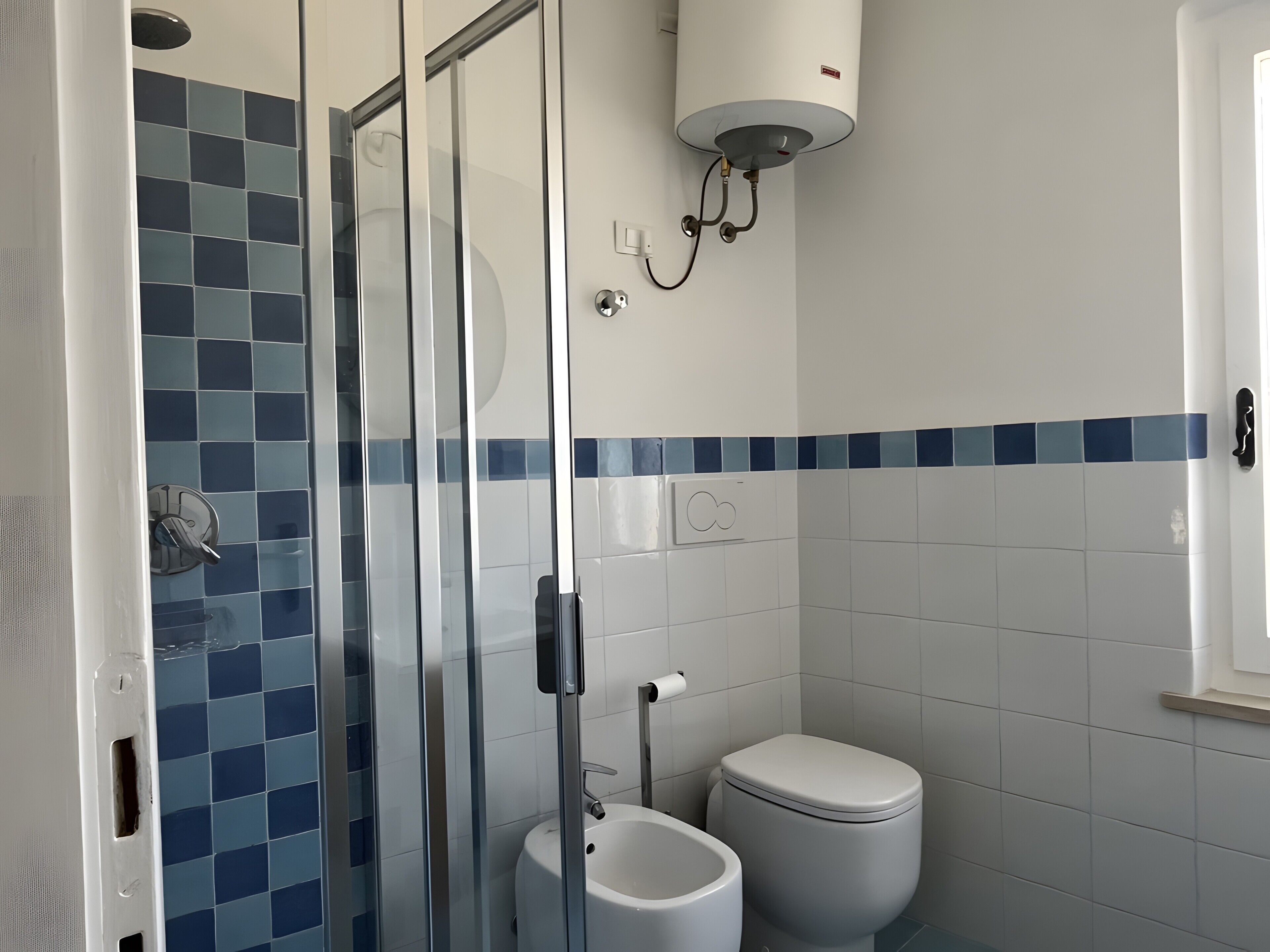 Un baño con cabina de ducha de vidrio, inodoro y calentador mural.