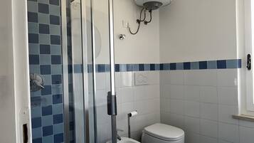 Un baño con cabina de ducha de vidrio, inodoro y calentador mural.