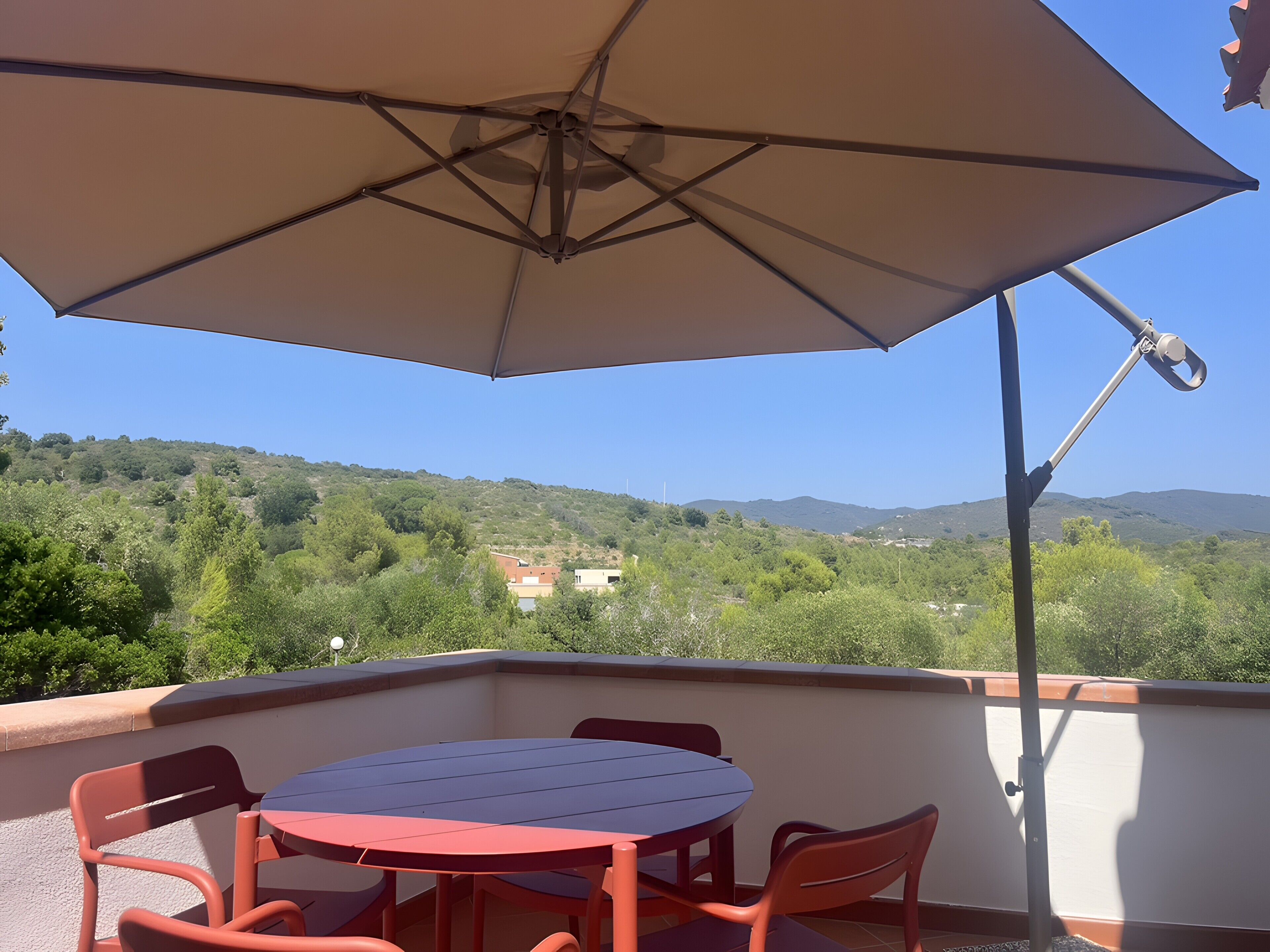 Un espace extérieur aménagé avec une table et des chaises, protégé par un grand parasol, et offrant une vue sur un paysage vallonné.