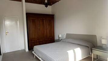 Un dormitorio con cama, mesita de noche, armario y ventilador de techo.