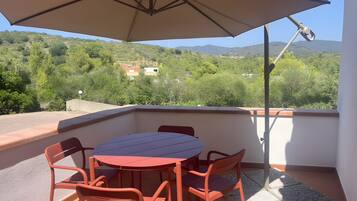 Un balcón con mesa y sillas, una sombrilla y vistas a un paisaje verde con colinas.