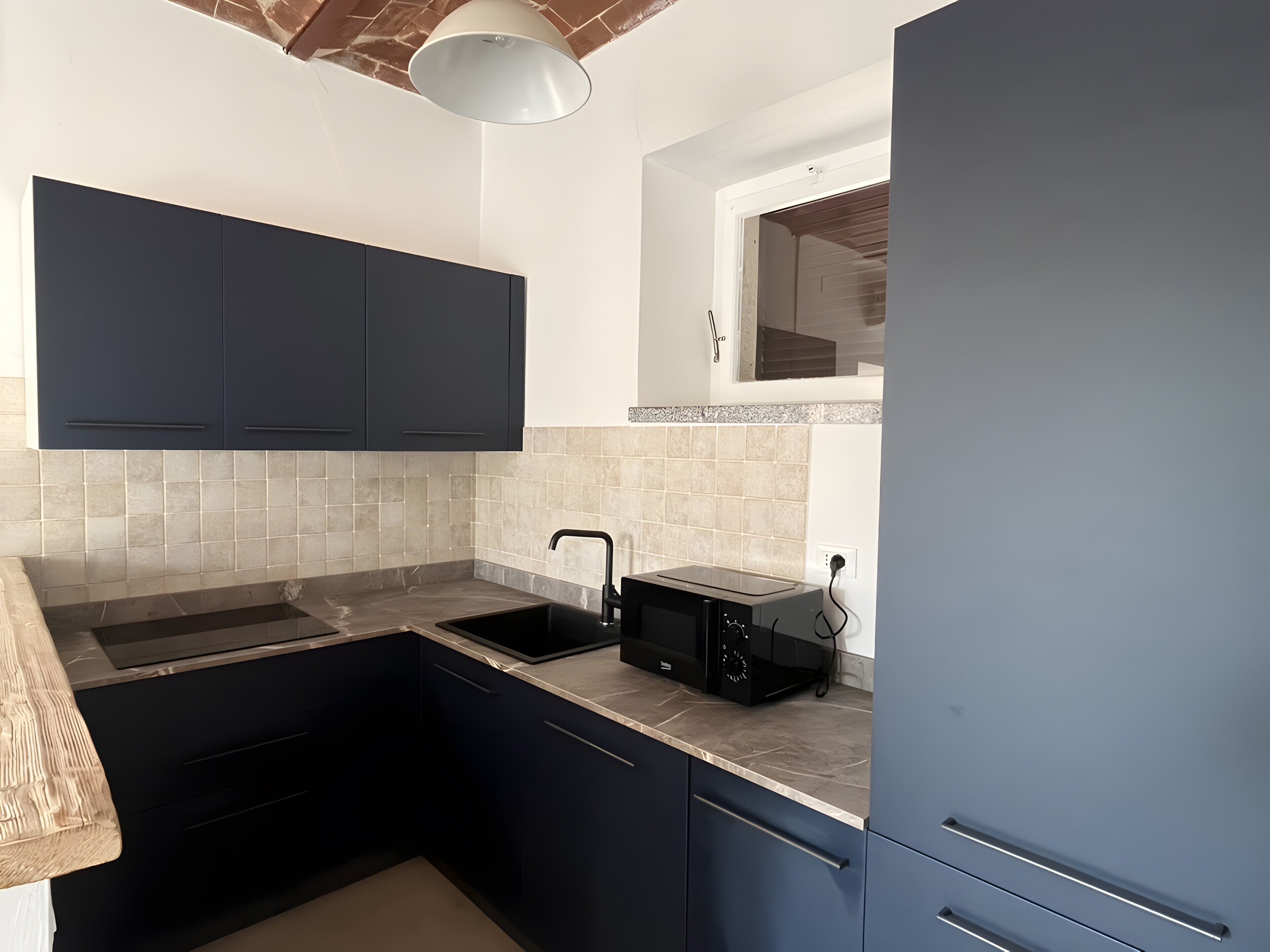 Una cocina con armarios oscuros, encimera, fregadero y microondas.