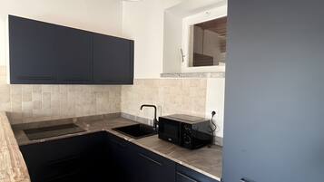 Una cocina con armarios oscuros, encimera, fregadero y microondas.