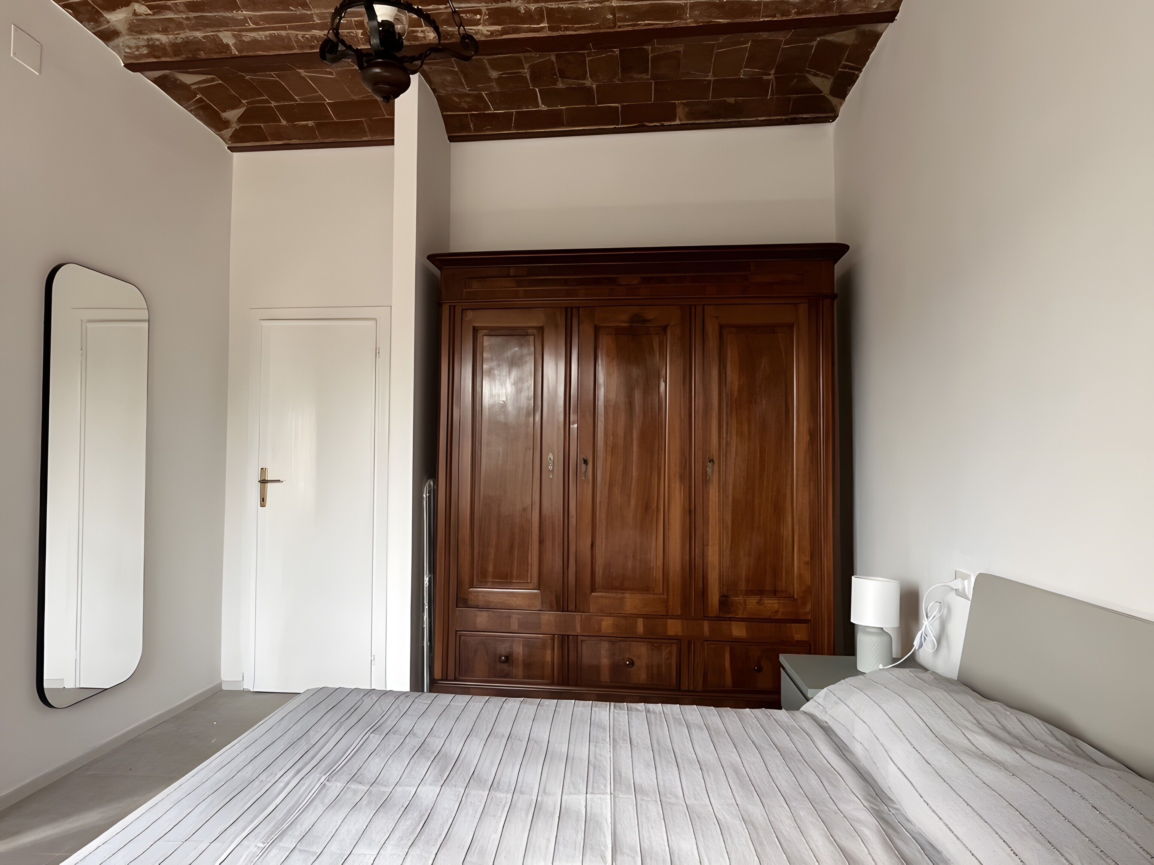 Une chambre à coucher avec un lit, une armoire, un miroir et une table de chevet.