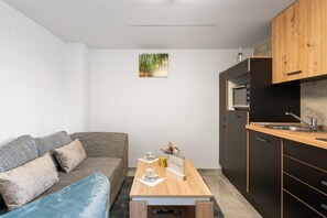 Ein kompakter Wohnraum mit Sofa, kleinem Tisch, Küchenzeile mit Spüle und einem Bild an der Wand.