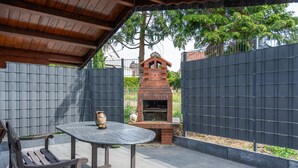 An outdoor patio with a brick barbecue grill, a metal table, and two wooden chairs. - Milser Hof · Apt. 1 – Cozy for 2 (Bielefeld)