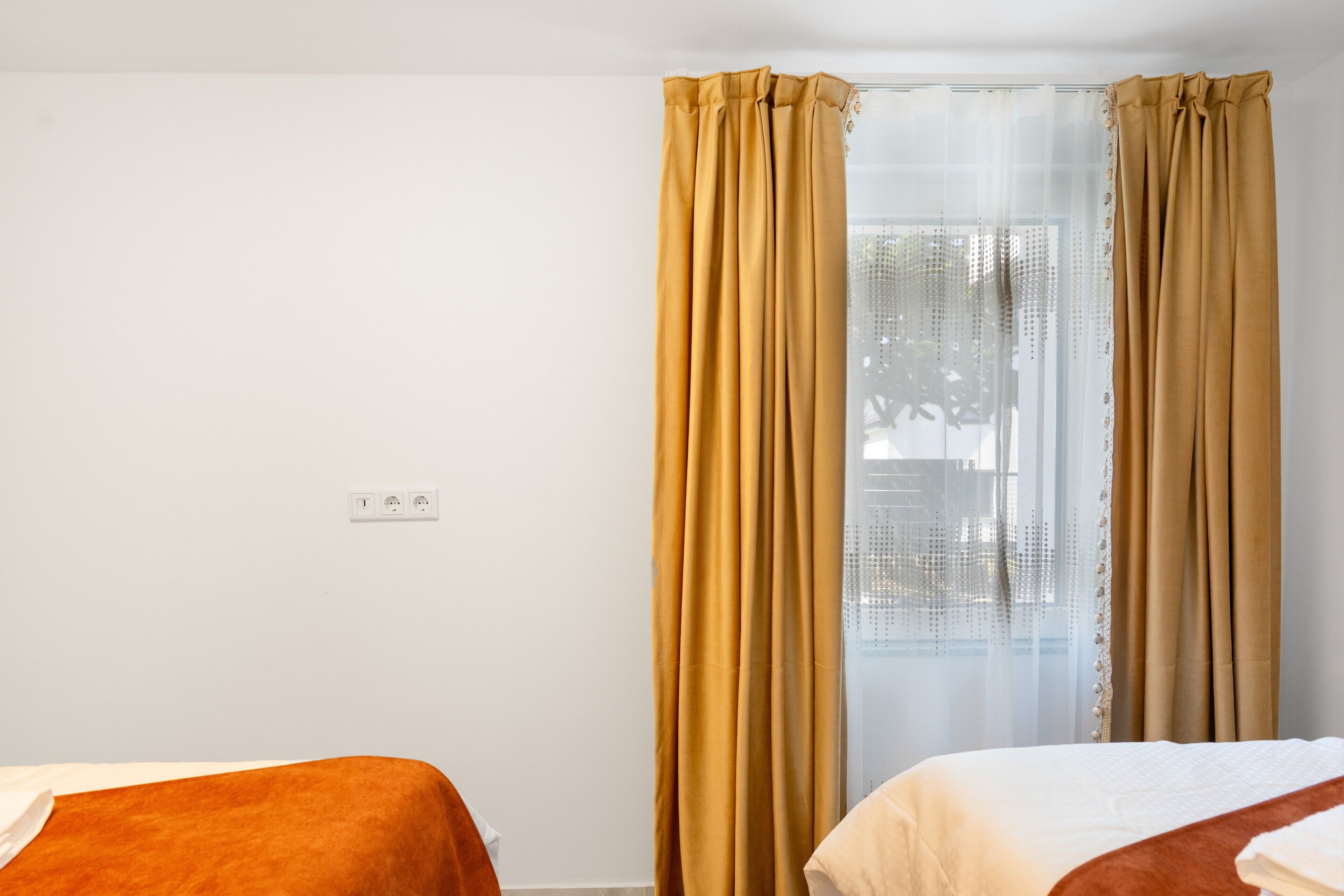 Quarto de hotel com duas camas, uma janela com cortinas finas e uma tomada na parede.