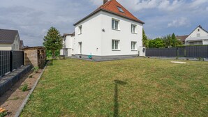 A two-story white house with a red-tiled roof, a fenced yard, and a small garden area. - Milser Hof · Apt. 1 – Cozy for 2 (Bielefeld)