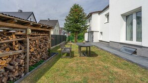A backyard with a wooden pergola, a table and bench, and a tall coniferous tree. - Milser Hof · Apt. 1 – Cozy for 2 (Bielefeld)