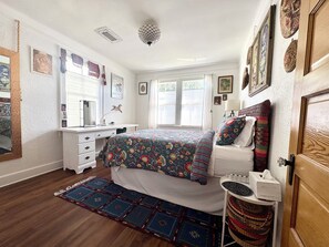 Ein Schlafzimmer mit Bett, Schreibtisch, Stuhl, Teppich und einer Tür.