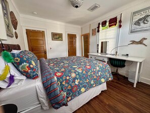 A bedroom with a bed, a desk, and a chair. There are doors, a mirror, and wall decorations. - Sweetest Spot in the Big Easy! Colorful 2/2 in fantastic walkable neighborhood! (New Orleans)