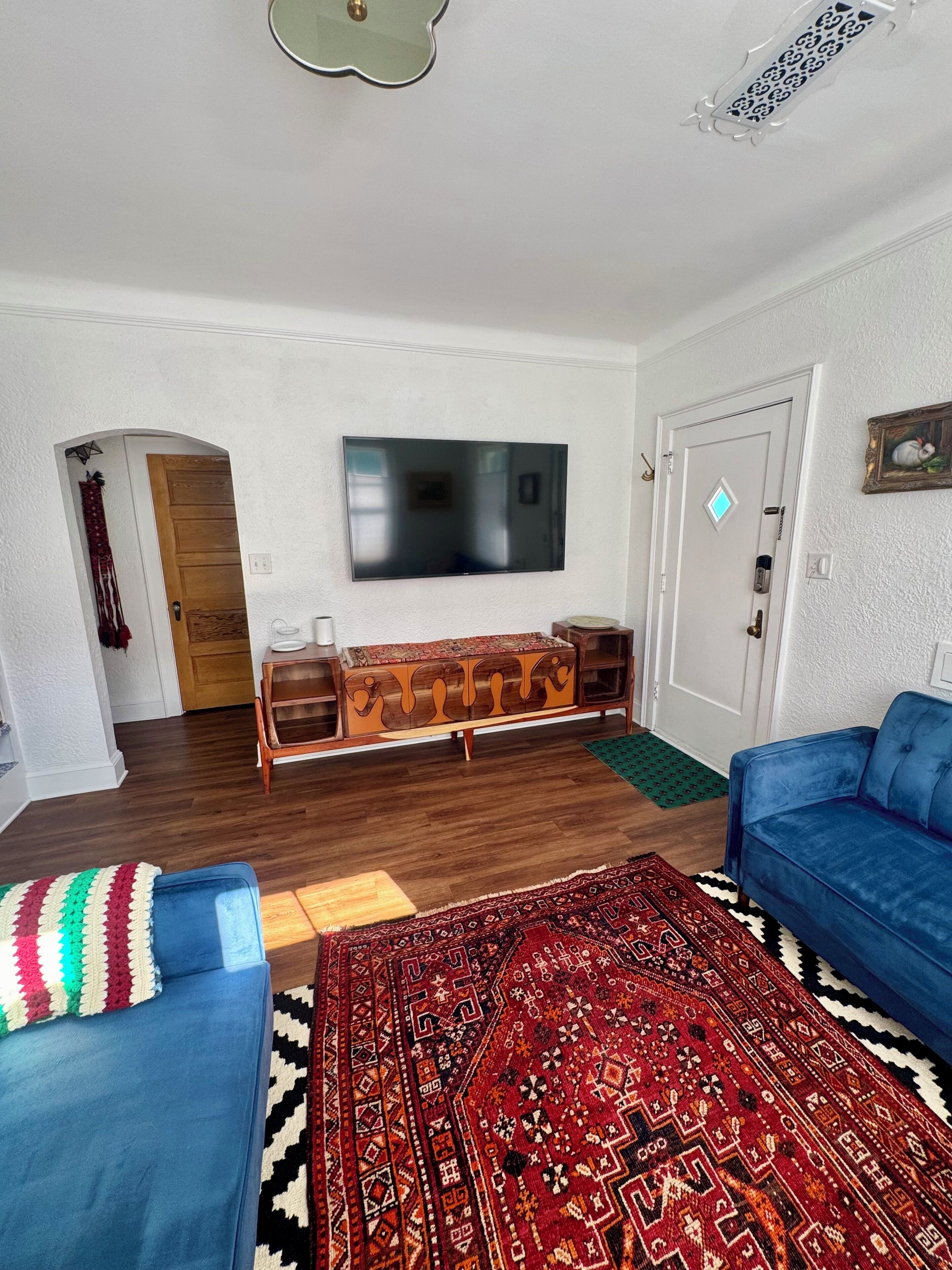 Una sala de estar con un televisor de pantalla plana, un mueble de madera, un sofá azul y un tapete estampado.