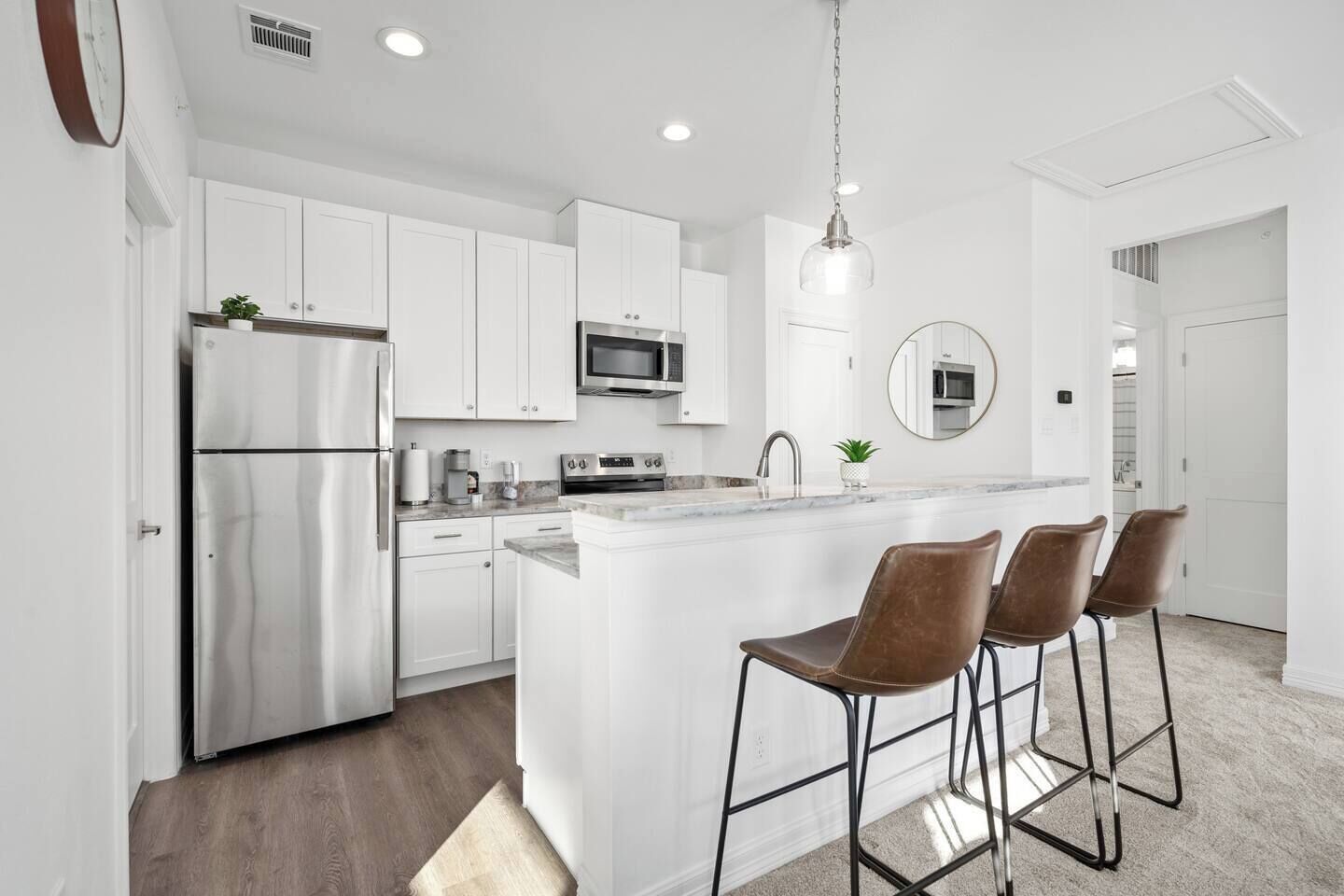 Una cocina moderna con armarios blancos, electrodomésticos de acero inoxidable y una isla central con taburetes de bar.