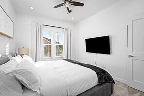 A hotel room with a bed, a television mounted on the wall, a ceiling fan, and a window with curtains. - New Build: B: 1BR/1BA Modern Condo in Houston (Houston)