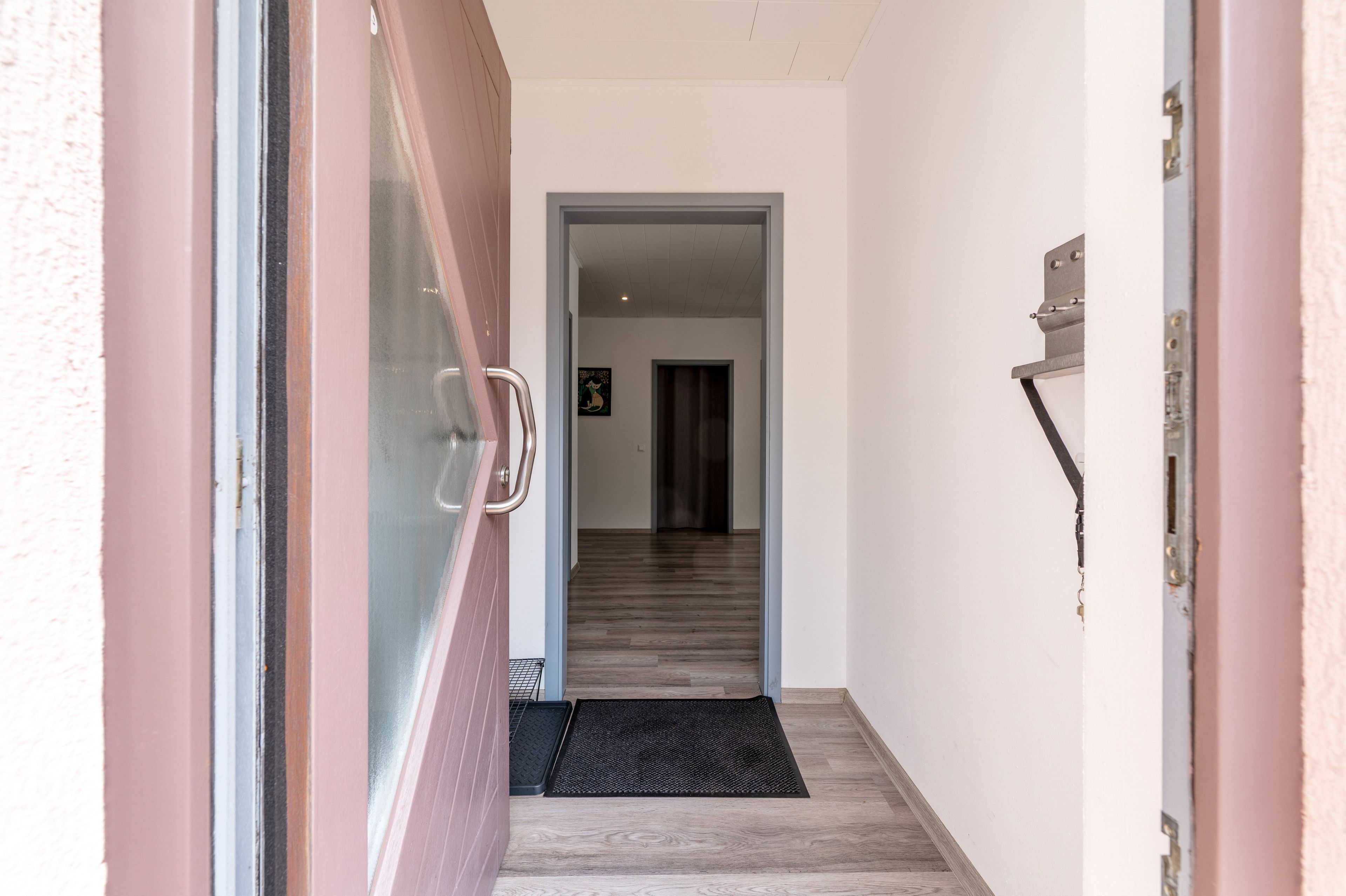 Um corredor com uma porta que dá para um quarto, um tapete de entrada e uma luminária fixada na parede.